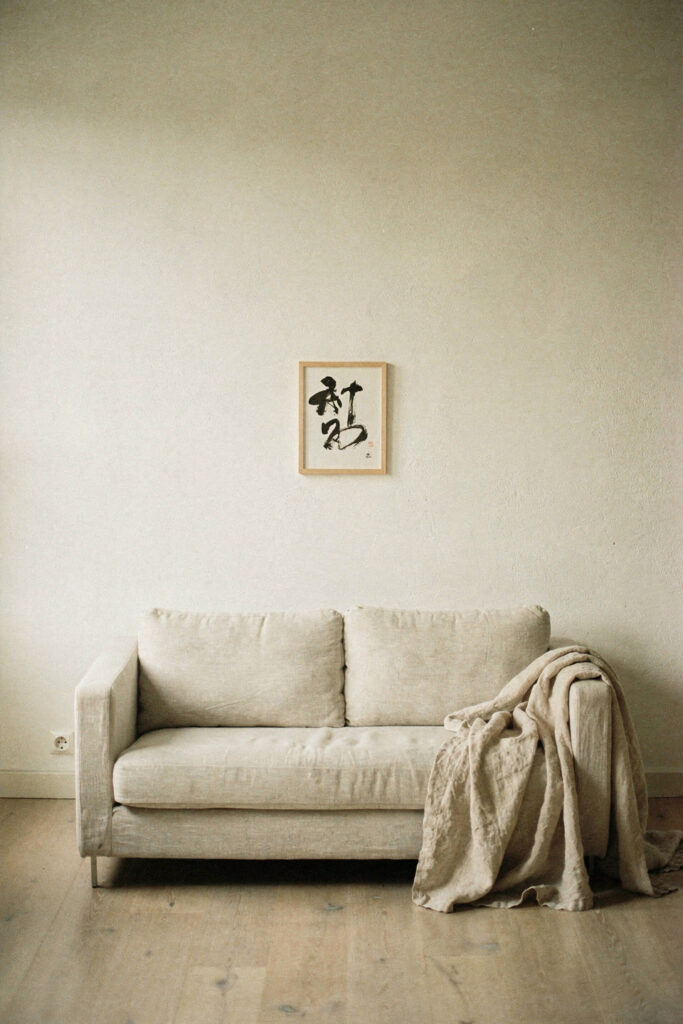 A low linen sofa against a warm white wall with around 40 percent of the wall left bare above it and one small ink piece hung low and off-center
