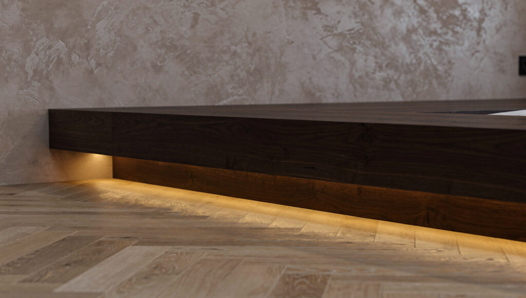 A side profile view of a dark walnut floating platform bed showing a 4-inch recessed shadow gap beneath the visible platform edge with a thin warm 2700K LED strip glowing softly within the gap, the heavy wooden platform appearing to hover above the light oak herringbone floor