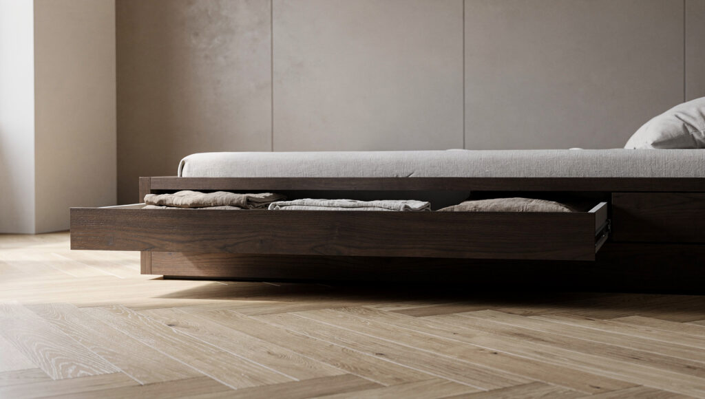 A low dark walnut platform bed at 16 inches height with one shallow integrated drawer partially open along its long side, the drawer front finished in matching walnut with a flush pull and approximately 5 inches of depth holding folded natural linen, the overall bed height remaining low-profile