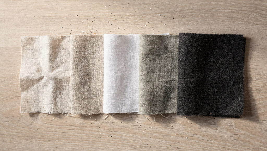 Five pale linen swatches — undyed, oat, flax, warm white, greige — with a deeper charcoal wool swatch set apart.