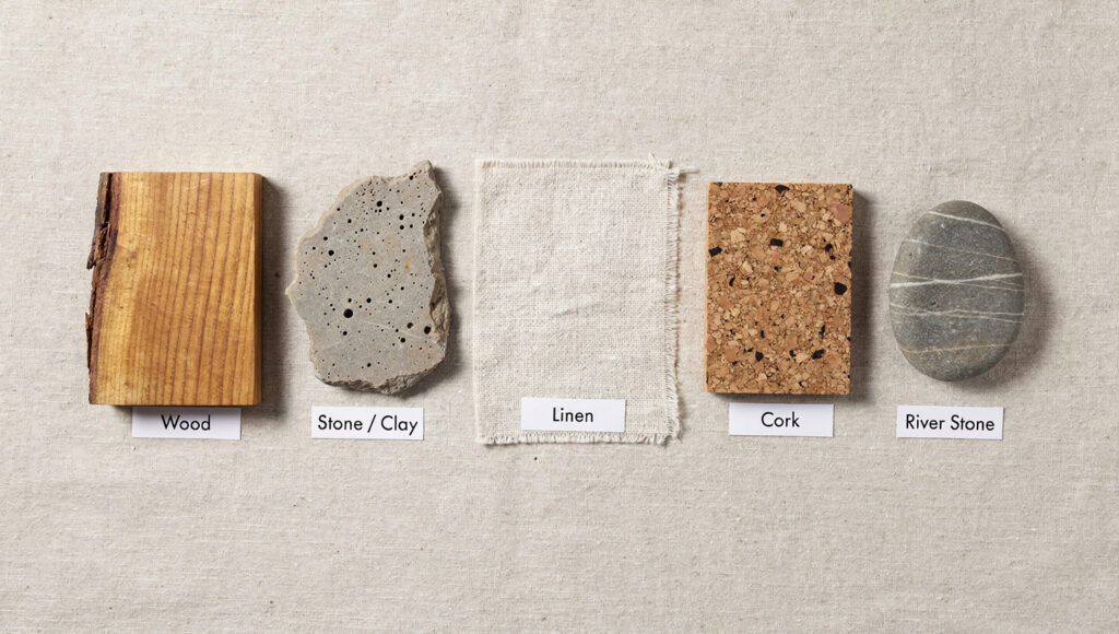 A biophilic materials flat lay on raw linen showing five samples arranged like a specification reference — live-edge wood with visible grain, a raw unglazed stone or clay fragment, undyed linen fabric, a cork panel sample, and a smooth river stone