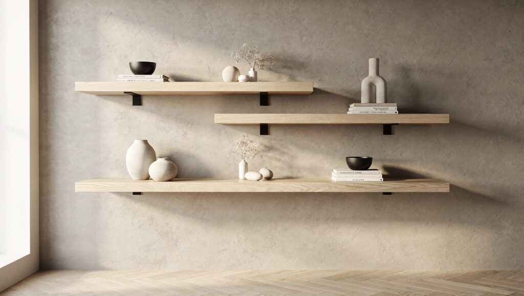 Three white oak floating shelves wall-mounted at varied heights on a warm greige limewash wall with the middle shelf offset slightly right creating organic asymmetry — each shelf styled with the three-zone composition method, slim matte black brackets barely visible, clear herringbone floor beneath