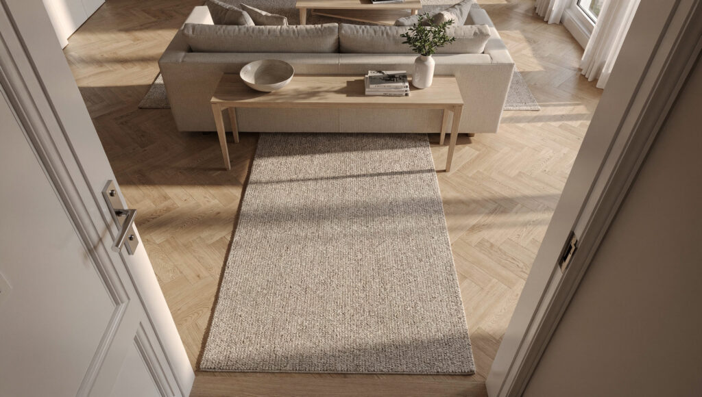 An elevated bird's eye view of a front door opening directly into an open living space showing a textured wool runner rug extending perpendicular from the door and a slim white oak console positioned to interrupt the direct sightline from the door to the sofa, demonstrating zone boundary creation without walls