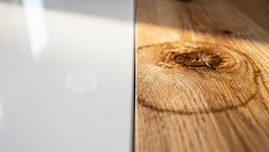 Macro of two tabletop finishes meeting at a seam: flat white lacquer on the left, oiled open-grain oak with a knot on the right