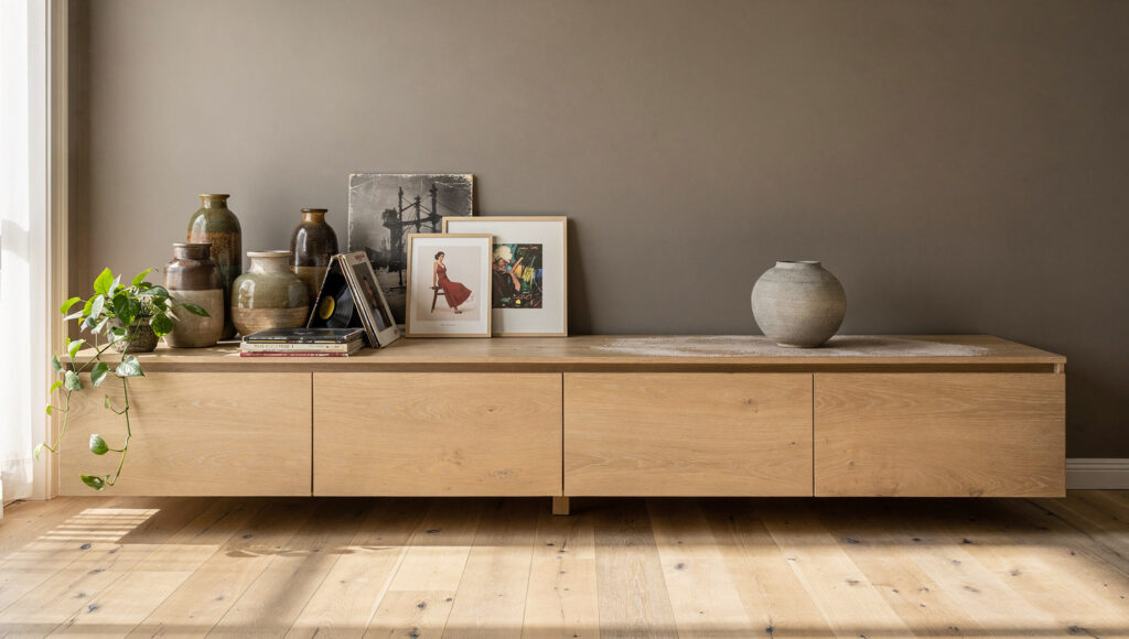 One long credenza with its left half crowded with ceramics records and framed prints, and its right half holding a single stoneware vessel.